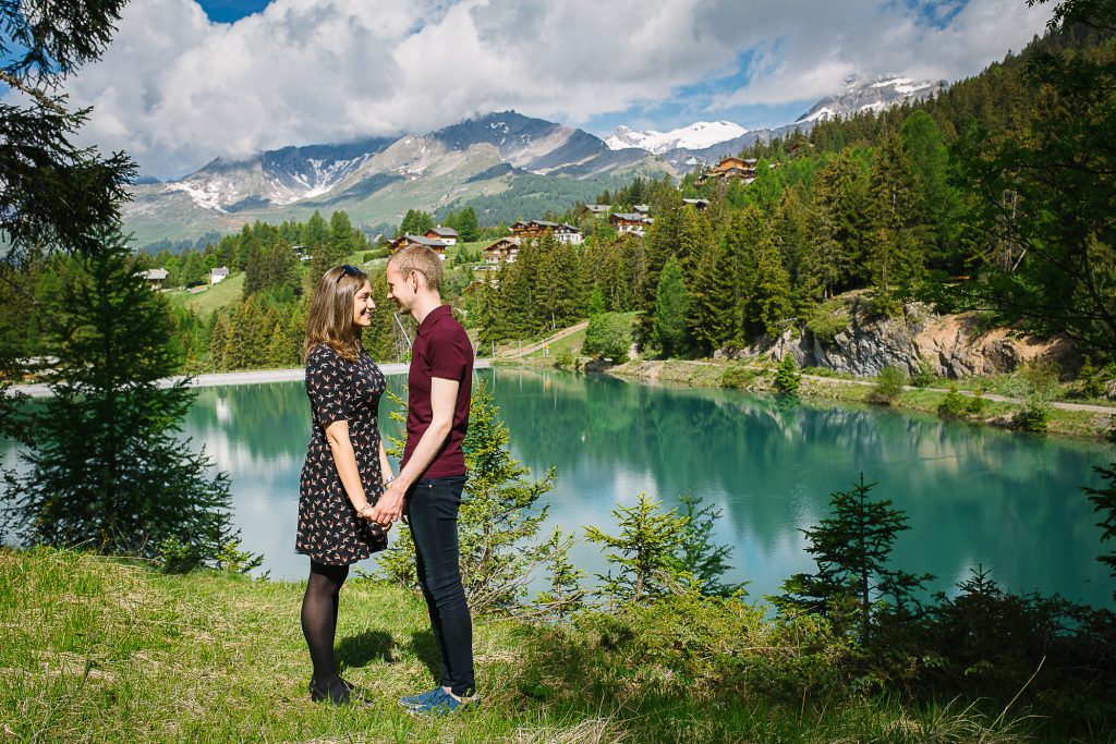 Young couple stand hand in hand by an Alpine lake